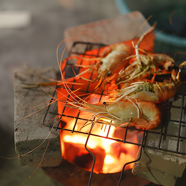 Large prawns grilling over an open flame on a rustic charcoal stove.