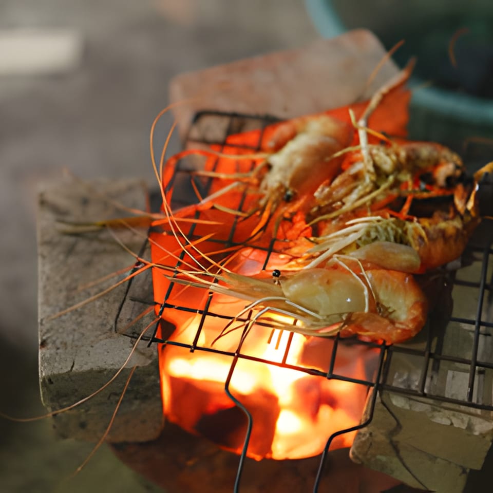 Large prawns grilling over an open flame on a rustic charcoal stove.