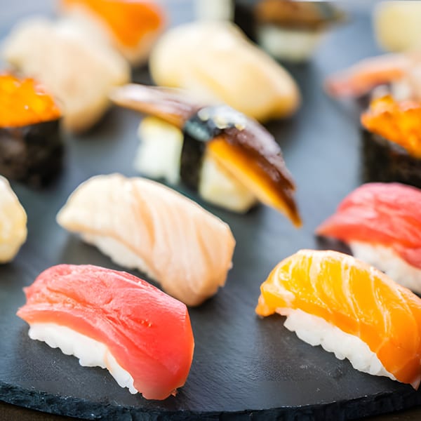 Assorted sushi and nigiri, including tuna, salmon, and eel, arranged on a dark slate board.