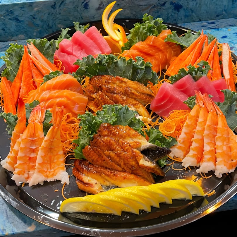 A large platter of sashimi, including tuna, salmon, shrimp, crab sticks, and eel, garnished with kale and lemon.