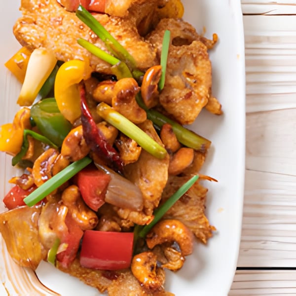 Close-up of a Thai dish with crispy chicken, cashews, bell peppers, and green onions.