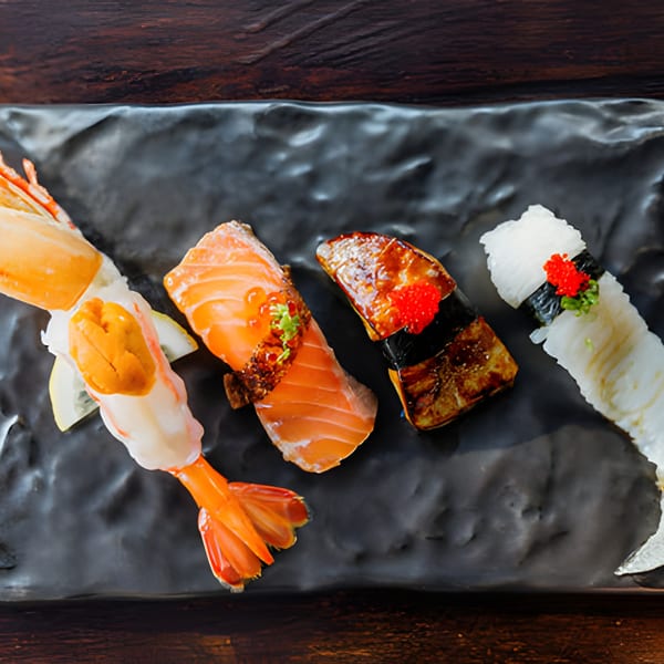 Four pieces of sushi, including shrimp, salmon, and eel, on a dark textured plate.