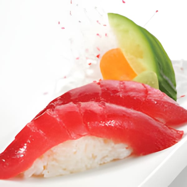 Two pieces of red tuna sushi with rice, garnished with cucumber, carrot, and wasabi.