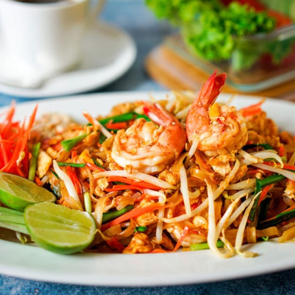 A white plate of BAITONG Thai Pad See Ew noodles with shrimp, lime, and vegetables.