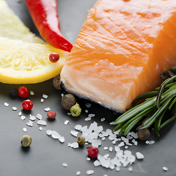 Salmon fillet with lemon, red chili, rosemary, peppercorns, and sea salt on a dark surface.
