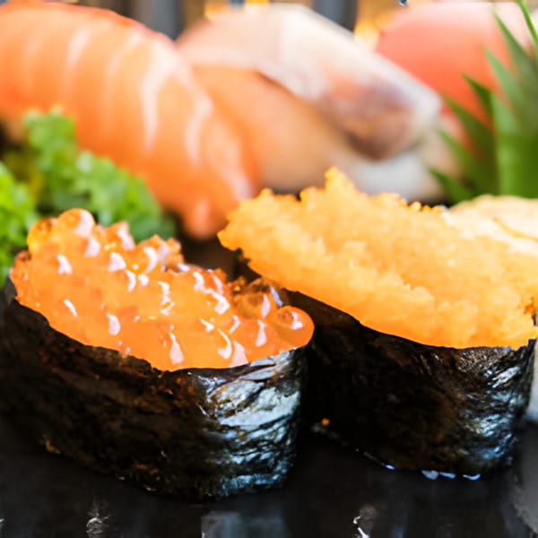 Close-up of two gunkan maki sushi, one with orange roe and another with yellow topping.