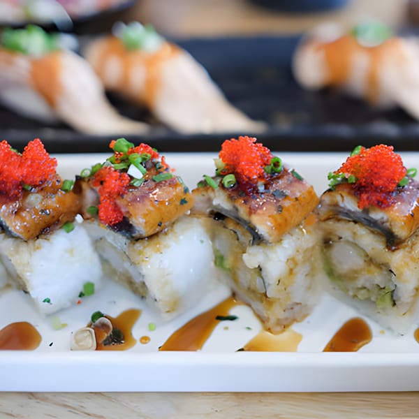 Four pieces of sushi with eel, red roe, and green onions on a white plate with sauce.