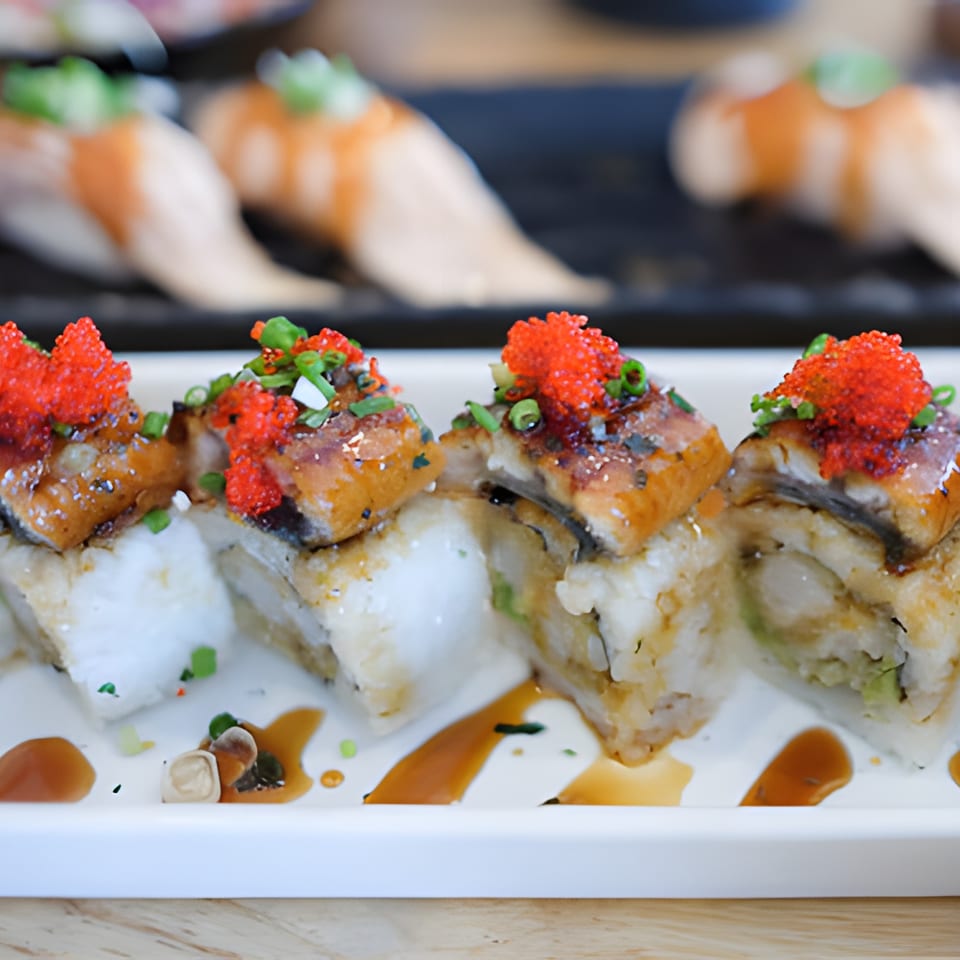 Four pieces of sushi with eel, red roe, and green onions on a white plate with sauce.